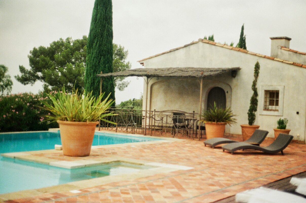 A swimming pool with terracotta patio, potted plants, and a house in Provence